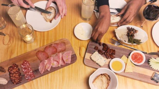Photo of people's hands eating from a table of charcuterie and other foods